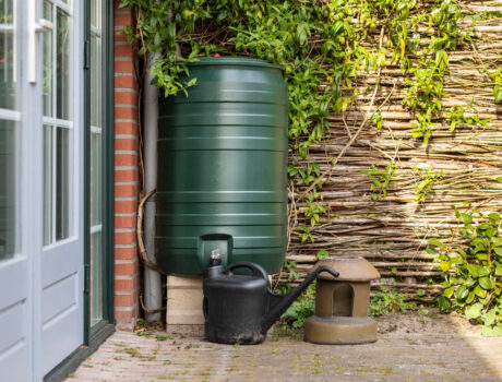 a homemade rain barrel sits against the exterior wall of a house in the yard.
