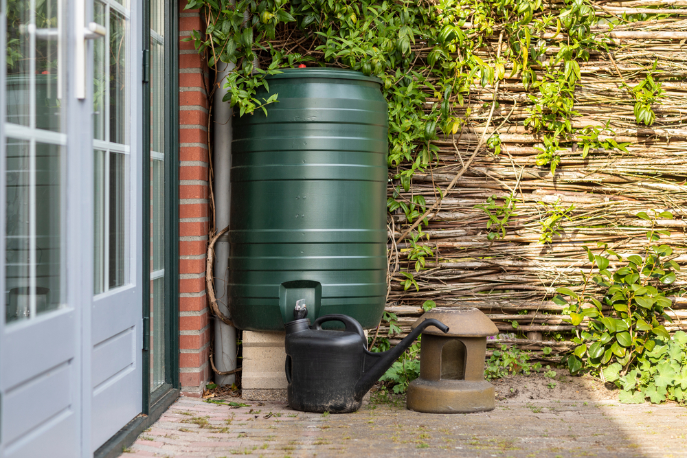 a homemade rain barrel sits against the exterior wall of a house in the yard.