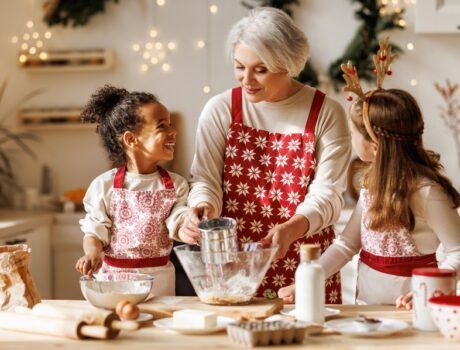 a grandmother and her two grandchildren dressed in Christmas apparel bake in the kitchen during the holidays